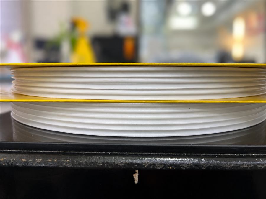 Side-view comparison of plastic spools: the upper stack without microcellular foaming shows shrinkage and warpage, while the lower stack with microcellular foaming is flat and dimensionally stable